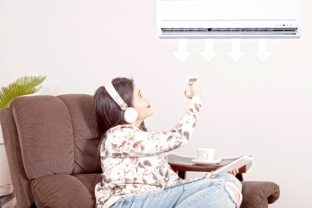 istock beautiful woman using remote control of air conditioner 1127356348