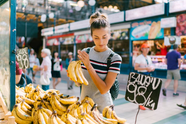 Young woman buying bananas at the market Tourist woman in Budapest buying fresh fruits agricultural fair stock pictures, royalty-free photos & images