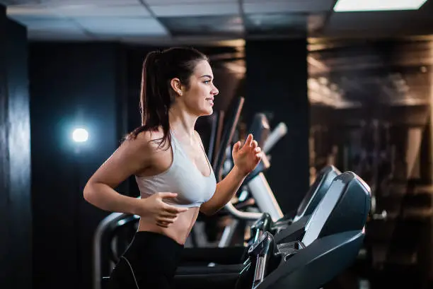 Young sports woman with ponytail working out in the gym, running on treadmill, side view.