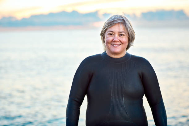 istock Obese woman in wetsuit smiling at beach 1127359021