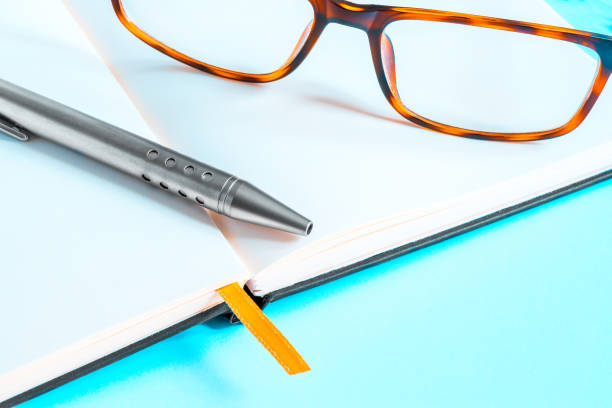 ein paar elegante brille und einem kugelschreiber auf eine offene notebook auf blauem hintergrund - personal organizer address book diary glasses stock-fotos und bilder