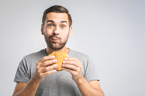 Young man holding a piece of hamburger. Student eats fast food. Burger is not helpful food. Very hungry guy. Diet concept.
