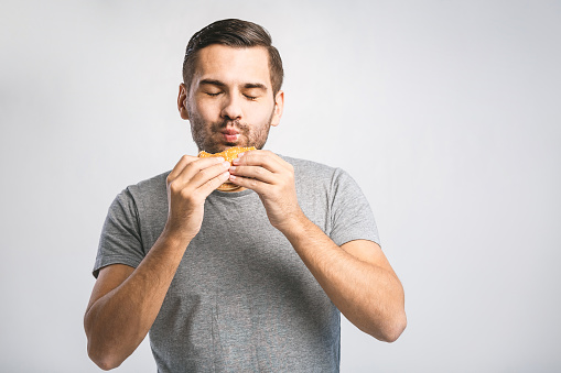 Young man holding a piece of hamburger. Student eats fast food. Hot helpful food. very hungry guy. Diet concept.