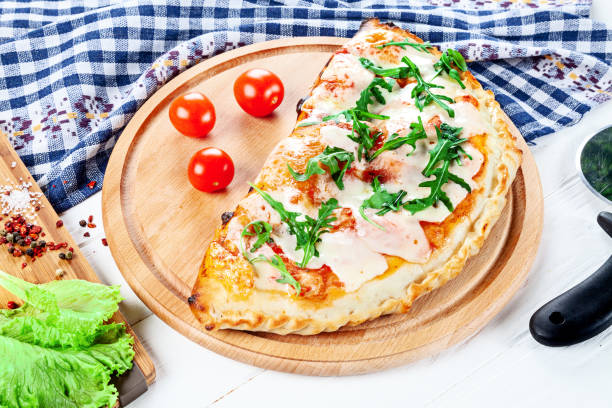 zbliżenie na calzone na pokładzie pizzy na białym tle z ziołami i przyprawami. restauracja, menu, przepis, koncepcja kawiarni. - pizza pastry crust stuffed cheese zdjęcia i obrazy z banku zdjęć