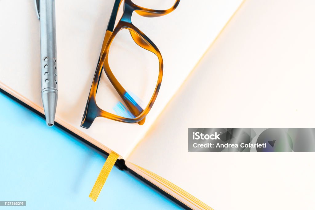 A pair of elegant eyeglasses and a ballpoint pen on an open notebook on a blue background Address Book Stock Photo
