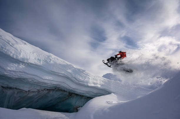 atleta realizando un paso adelante salto sobre una moto de nieve - motoesquí fotografías e imágenes de stock