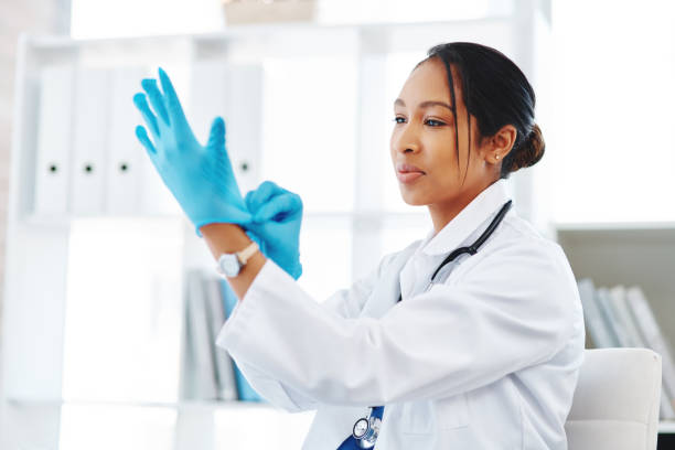 Hygiene is everything in a hospital Shot of a young doctor putting on surgical gloves in a hospital putting on latex gloves stock pictures, royalty-free photos & images