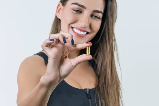 jovem bela mulher saudável no sportswear com vitamina d, e, a sorrir um óleo de peixe omega-3 cápsulas, sobre fundo branco - vitamin pill nutritional supplement capsule antioxidant - fotografias e filmes do acervo