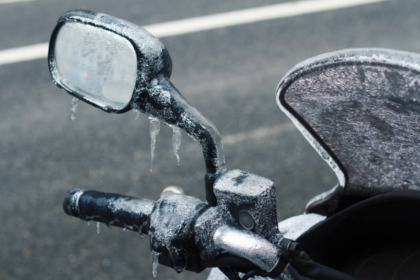 rear view closeup of motorcycle frozen windshield handlebar and rear mirror covered in icicles during wintertime with city street in the foreground