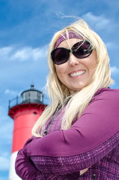Portrait of a beautiful blonde woman, smiling with her arms crossed in front of Nauset Lighthouse on Cape Cod