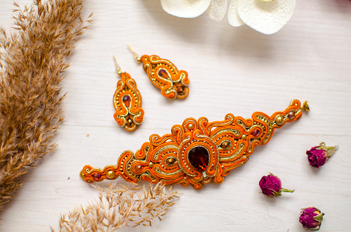 Beaded braselet and earrings set. Orange soutache jewelry with flowers on the white wooden background. Women accessories