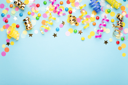Birthday party background on blue. Top view. Border made of colorful serpentine, candies and confetti.