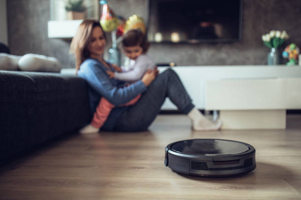 Robotic Vacuum Cleaner Cleaning While Mother and Daughter Playing Robotic Vacuum Cleaner Cleaning Floor While Mother and Daughter Playing on the sofa smart home family stock pictures, royalty-free photos & images