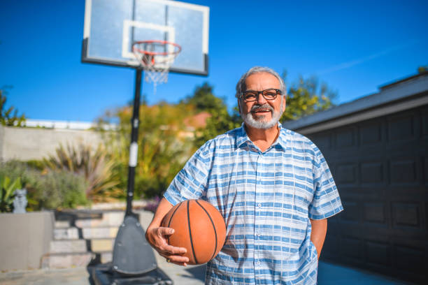 lächelnder senior mann hält basketball im hinterhof - basketball basketball hoop california southern california stock-fotos und bilder