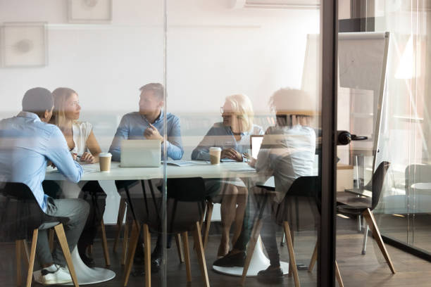 Business people negotiating at boardroom behind closed doors Advertising department brainstorming at modern office boardroom behind closed doors, view through the glass wall. Diverse staff led by ceo discussing new project sharing ideas thoughts and sales pitch pictures of people thinking stock pictures, royalty-free photos & images