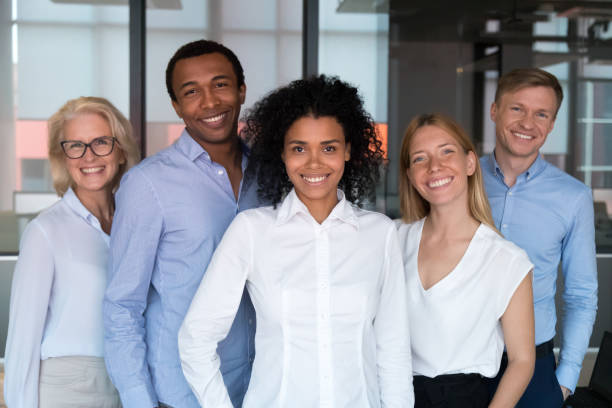 Black team leader photographing with workmates in office Attractive successful people standing together smiling posing looking at camera feels proud and satisfied. Multi-ethnic businesspeople led by afro mixed race woman photographing in modern office room serving sport stock pictures, royalty-free photos & images