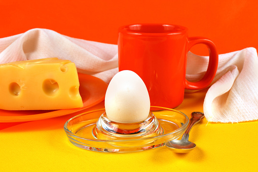 Still life with egg, cheese and orange mug on white towel background