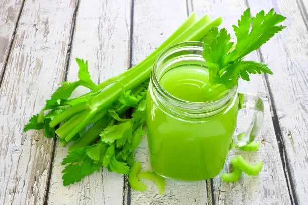 Celery juice in a mason jar glass. Downward view over a rustic white wood background.