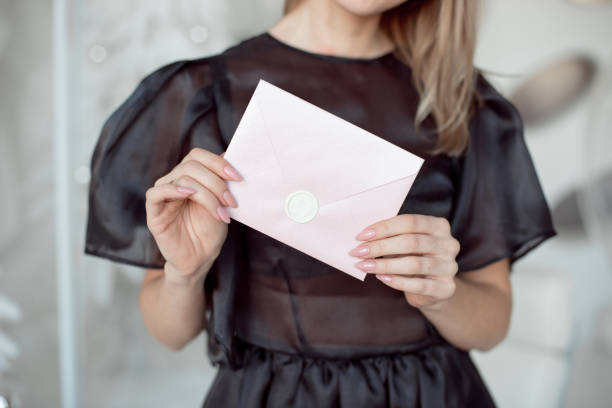 nahaufnahme foto einer frau hände halten einen rosa einladung umschlag mit einem wachs-siegel, ein geschenk-gutschein, eine karte, eine hochzeit einladungskarte. - bride caucasian wedding ceremony close up stock-fotos und bilder