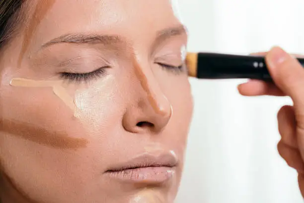 Make up artist applying liquid face powder foundation to a female client's face and blending contours
