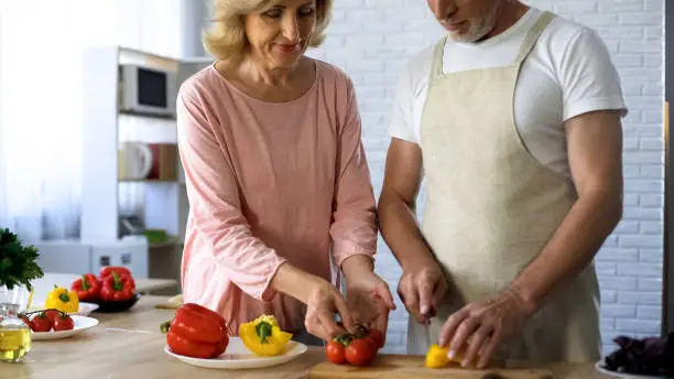 Senior man and loving wife cooking healthy vegetable lunch in kitchen, family