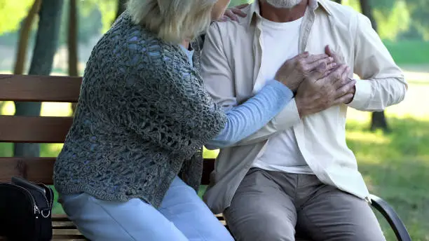 Pensioner suffering heart pain, walking in park, scared wife supporting him