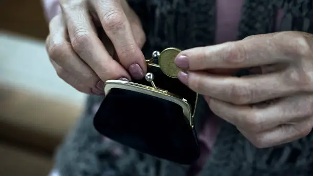 Grandmothers trembling hand putting coin in wallet, pensioner poverty, closeup