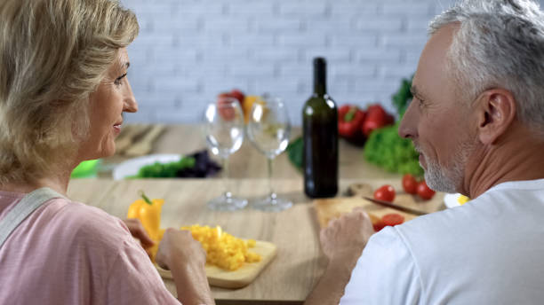 istock Aged female and male looking each other while cooking meal, cutting vegetables 1127406656