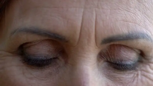 Closed eyes of wrinkled old woman, eyebrows and eyelids tattoo, beauty concept