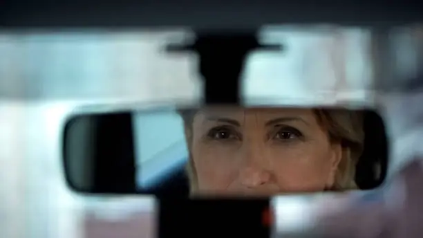 Old lady looking at her reflection in rear view mirror, car purchase, test drive