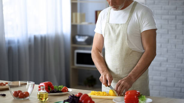 istock Elderly man in apron cutting fresh salad in kitchen, cooking tips, leisure hobby 1127407899