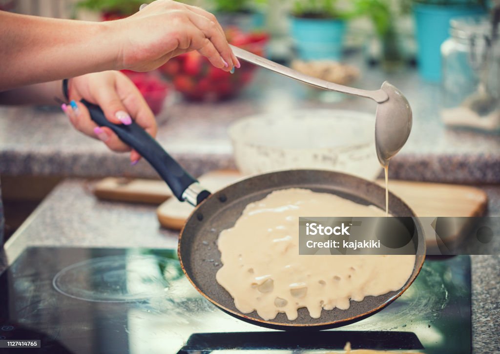 Woman Preparing Crepes Young woman making crepes at home, she pouring dough into frying pan Crêpe - Pancake Stock Photo