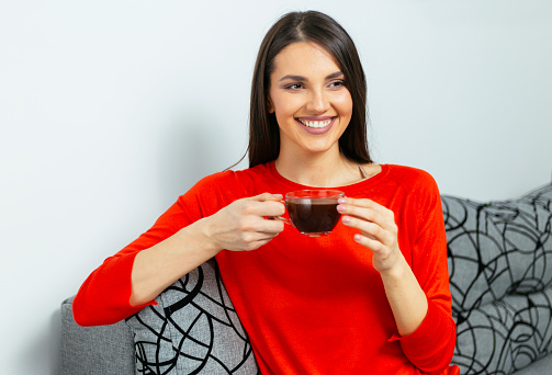 Portrait of beautiful woman sitting on sofa and holding cup of coffee while smiling