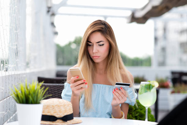 Beautiful girl cafe summer. Hand, plastic card and phone. Woman pays lunch or credit through online banking. Unhappy with price, disappointment with write-off of money. Upset and surprise purchase. stock photo