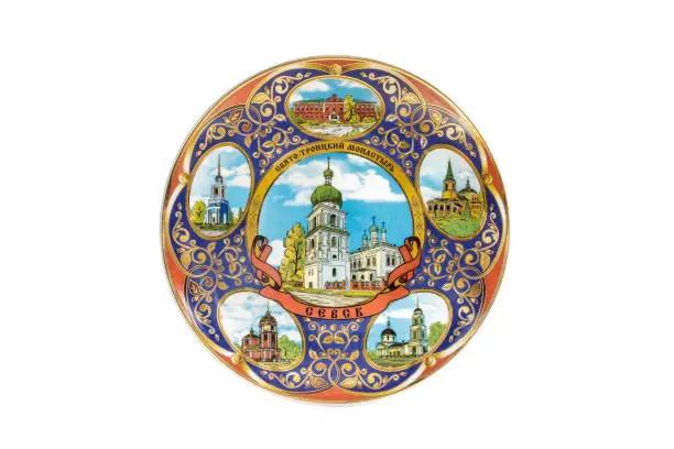 ceramic souvenir toy in the form of plate with beautiful color painting on isolated white background reflecting the national Russian culture with the inscription in Russian: Holy-Trinity monastery in the city of Sevsk