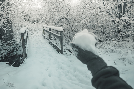 blurred hand with snowball in front of snow covered wooden bridge