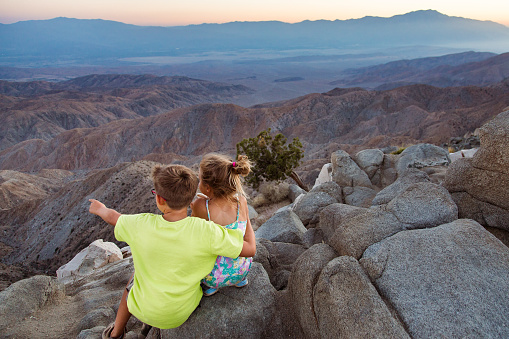 A brother points to the beautiful twilight panorama of the San Andreas Fault from Keys View in Joshua Tree National Park, to show his sister.