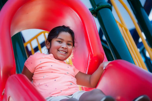 A happy and energetic girl playing on a red playground slide, about to slide down. stock photo