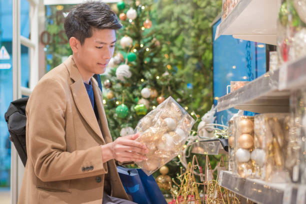istock Young asian man using cellphone and looking for christmas gift while shopping for christmas in mall or department store 1127446504