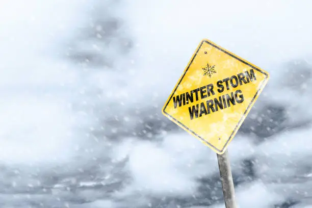 Winter storm season with snowflake symbol sign against a snowy background and copy space. Snow splattered and angled sign adds to the drama.