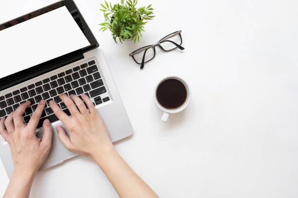 istock Man typing on laptop computer with white blank screen over white office desk table with cup of coffee. Top view with copy space, flat lay. 1127454133