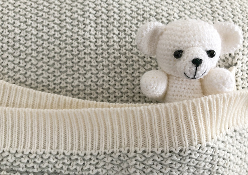 Small knitted toy bear hiding in the pocket of warm blanket. Soft toy bear. Hygge.
Cute teddy bear covered with a warm blanket