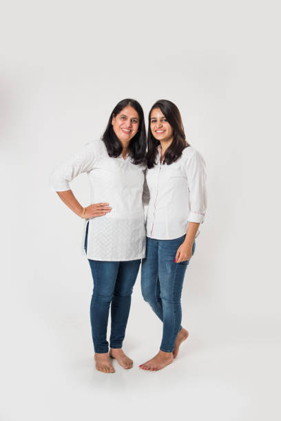 istock Indian old mother with young Daughter standing isolated over white background, while wearing white top and blue jeans. selective focus 1127457770