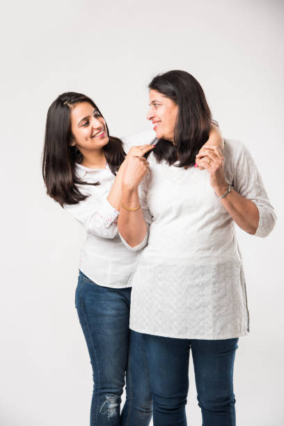 istock Indian old mother with young Daughter standing isolated over white background, while wearing white top and blue jeans. selective focus 1127458330