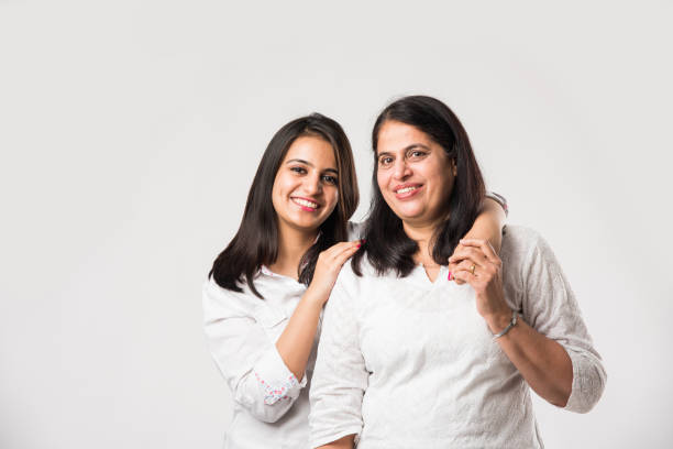 Indian old mother with young Daughter standing isolated over white background, while wearing white top and blue jeans. selective focus