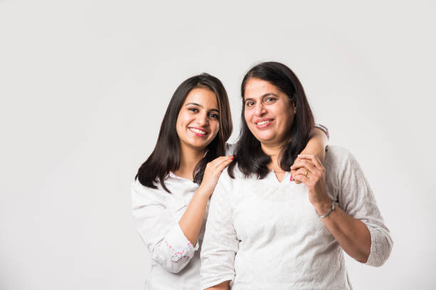 indyjska stara matka z młodą córką stojącą odizolowaną na białym tle, ubrana w biały top i niebieskie dżinsy. selektywne skupienie - offspring family love india zdjęcia i obrazy z banku zdjęć