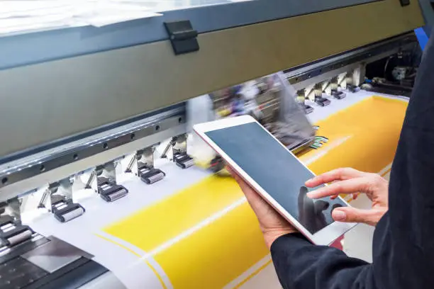 Photo of Technician touch control tablet on format inkjet printer during yellow vinyl