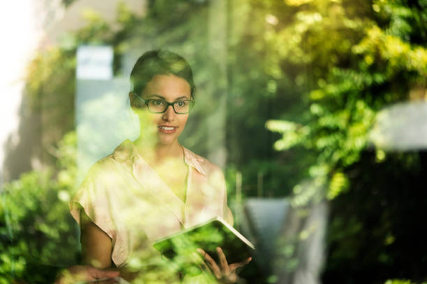 Thoughtful businesswoman seen through window A photo of thoughtful businesswoman seen through glass window. Female professional is holding diary. She is wearing formals in office. think green stock pictures, royalty-free photos & images