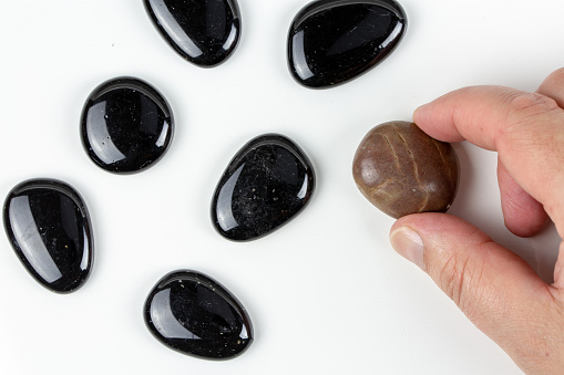 Black pebbles on white background with brown pebble. Concept of diversity or singularity