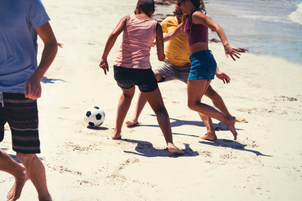 istock Young friends playing soccer on shore at beach 1127477253